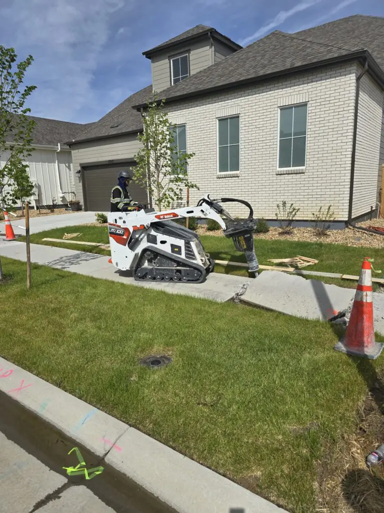 Small excavator breaking concrete sidewalk.